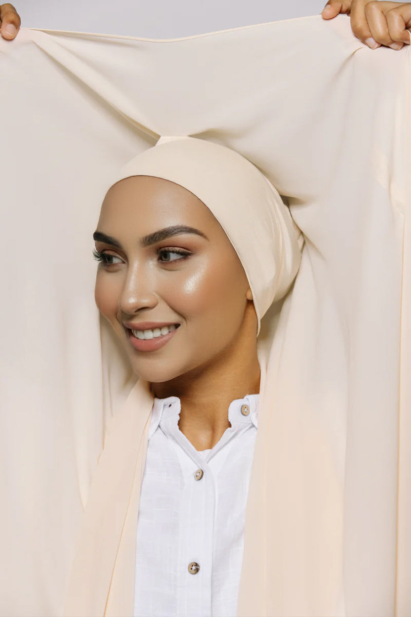 A woman wearing a beige chiffon hijab matching sewn undercap