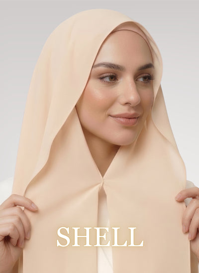 Woman wearing shell beige Nuramira instant chiffon hijab with front panels held by magnets and smooth drape in white studio