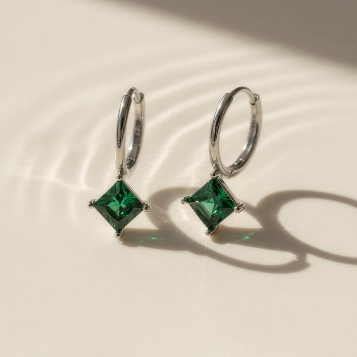 Amara drop earrings in emerald on neutral surface with soft studio lighting
