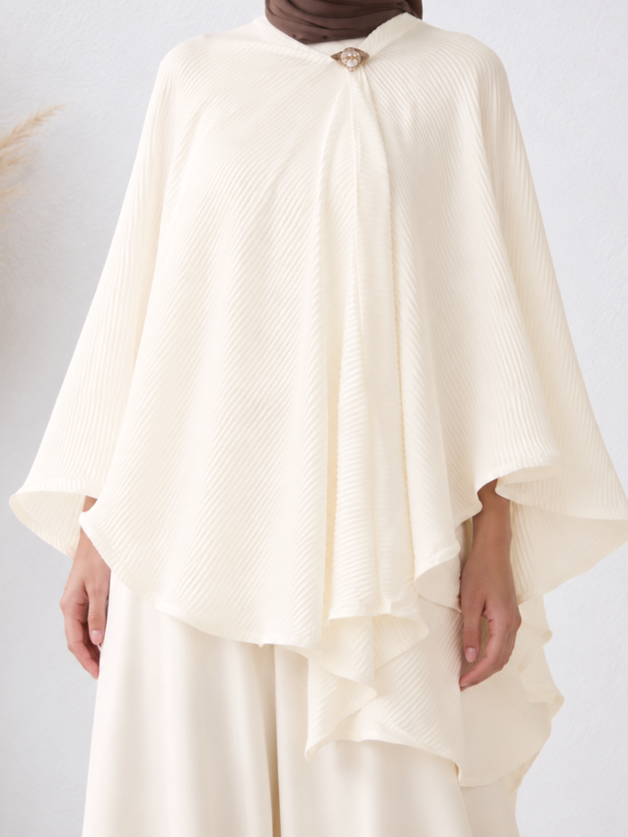 Close-up of the pleated cape with a gold brooch at the neckline.
