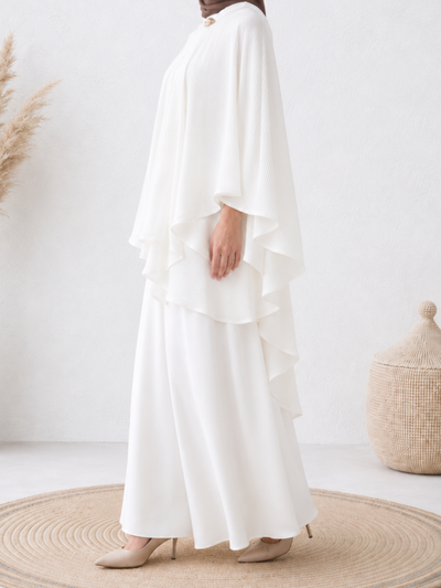 Side profile of a woman wearing the Elara™ Pleated Cape Set, displaying the layered pleated cape and fluid silhouette.
