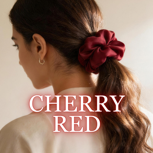 A woman wearing a cherry red satin scrunchie with wavy brunette hair, white background