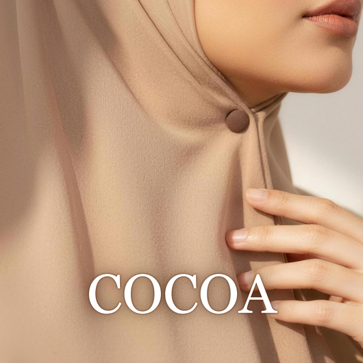 Close-up of a model wearing a beige hijab secured under the chin with a matte cocoa brown magnet, with her hand resting near her neck and the text "COCOA" overlaid at the bottom.