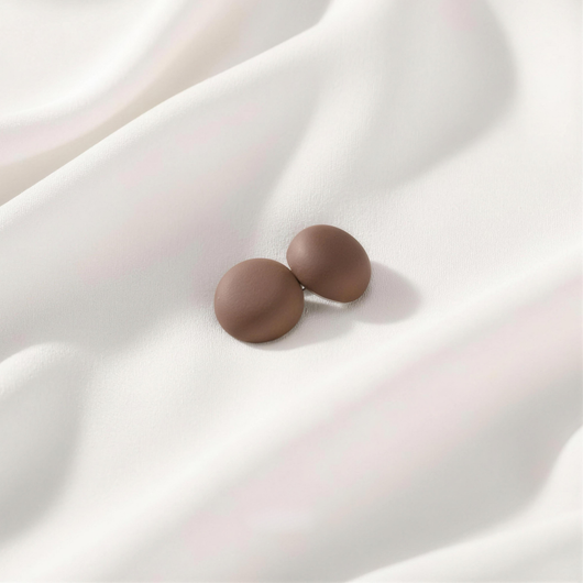 A pair of matte, rich cocoa brown round magnetic hijab pins displayed on a soft, draped white fabric backdrop.