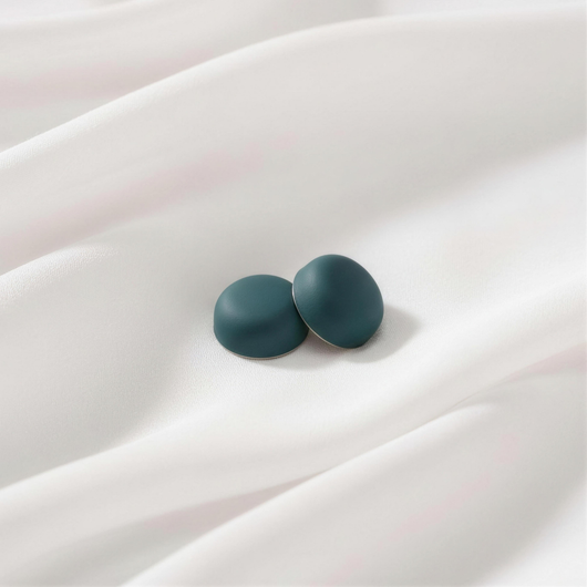 A pair of matte, deep emerald green round magnetic hijab pins resting together on a flowing white fabric background.