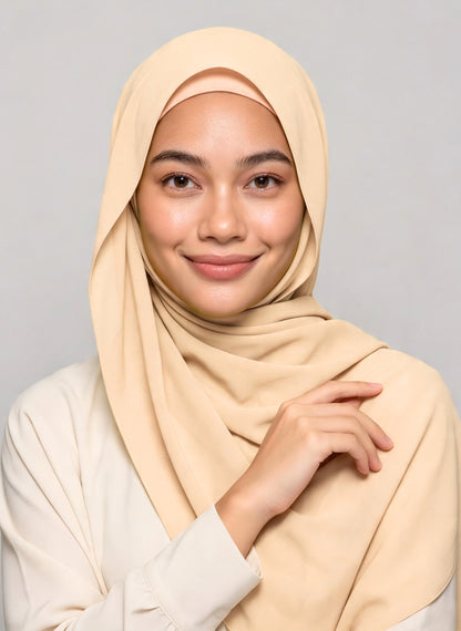 Hijabi woman wearing shell beige NurAmira instant chiffon hijab with soft drape over the shoulder and secure undercap against white studio smiling